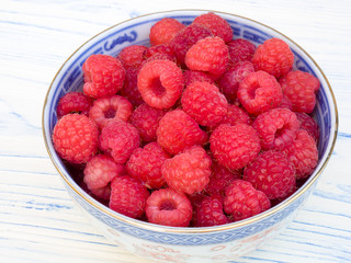 
Fresh raspberries in a blue china bowl, set on a white wooden board