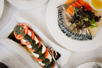 Закуска из помидор, соуса песто, сыра и рыбы на столе в ресторане 