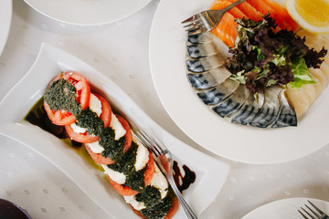 Закуска из помидор, соуса песто, сыра и рыбы на столе в ресторане 