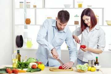 Loving smiling couple preparing healthy salad of fresh vegetables in  kitchen