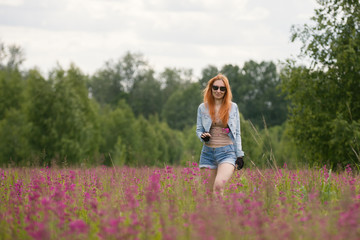 Beautiful red-haired girl walking on a flower meadow