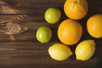 Fresh lemons, limes and oranges on brown wooden table. Juicy fruits.