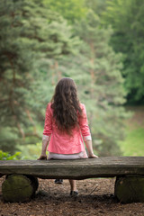 Junge Frau sitzt auf Parkbank mit dem R&uuml;cken zur Kamera