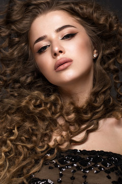 Beautiful brunette girl in move with a perfectly curly hair, and classic make-up. Beauty face. Picture taken in the studio on grey background.
