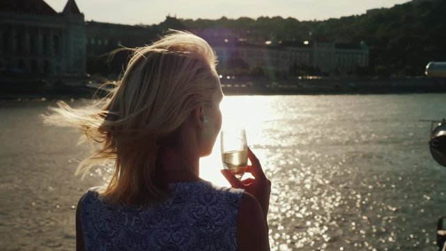 Enjoy river cruises on the Danube. A woman with a glass in her hand looks at the shoreline of Budapest