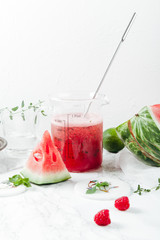 Pitcher with refreshing watermelon and strawberry lemonade with lime juice, ginger and honey on marble table and white background. Summertime beverage concept. Copy space