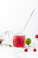 Pitcher with refreshing watermelon and strawberry lemonade with lime juice, ginger and honey on marble table and white background. Summertime beverage concept. Copy space