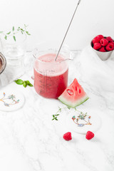 Pitcher with refreshing watermelon and strawberry lemonade with lime juice, ginger and honey on marble table and white background. Summertime beverage concept. Copy space