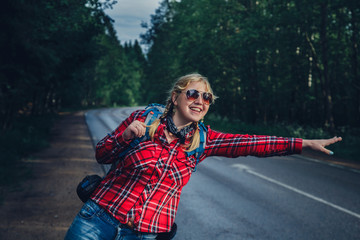 Lonely girl hitchhiking on the road with a backpack.