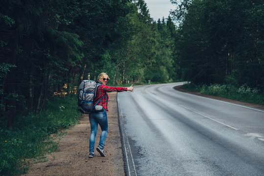 Lonely girl hitchhiking on the road with a backpack.
