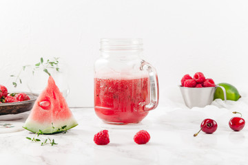Glass jar cup with refreshing watermelon and strawberry lemonade with lime juice, ginger and honey on marble table and white background. Summertime beverage concept. Copy space
