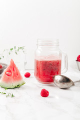 Glass jar cup with refreshing watermelon and strawberry lemonade with lime juice, ginger and honey on marble table and white background. Summertime beverage concept. Copy space