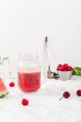 Glass jar cup with refreshing watermelon and strawberry lemonade with lime juice, ginger and honey on marble table and white background. Summertime beverage concept. Copy space