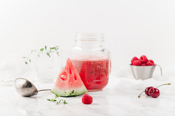 Glass jar cup with refreshing watermelon and strawberry lemonade with lime juice, ginger and honey on marble table and white background. Summertime beverage concept. Copy space