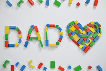 colorful wooden toy blocks lettering the word DAD and a heart on white background