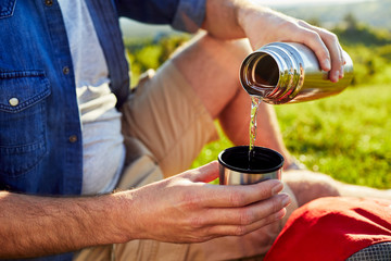 Close-up of a man pouring water into thermos cup