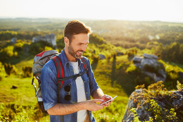 Handsome middle aged hiker using phone to check map while hiking