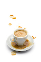 full cup of coffee with coffee spilled on the saucer and on the white table.