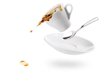 Zelfklevend Fotobehang cup of coffee spils with saucer and spoon and coffee falls on white background © winston