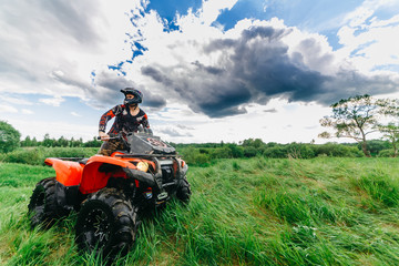Man on the ATV Quad Bike in a field. Blue sky with clouds.