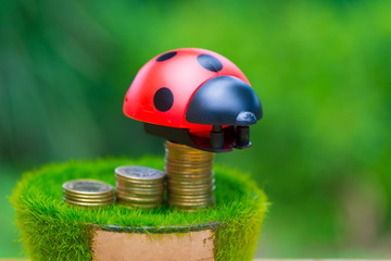 Stack of gold coin on artificial grass in pot, on wooden table with green nature background.