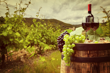 Fototapeta na wymiar Red wine bottle and wine glass on wodden barrel. Beautiful Tuscany background
