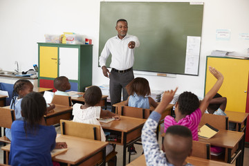 Teacher and kids with hands up in an elementary school class