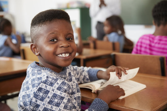 Boy at desk smiling to camera in an elementary school lesson