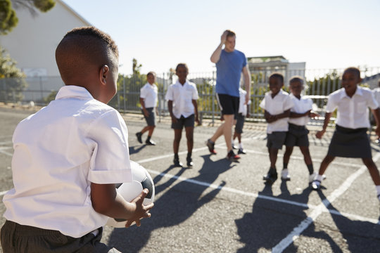 Teacher Plays Football With Young Kids In School Playground