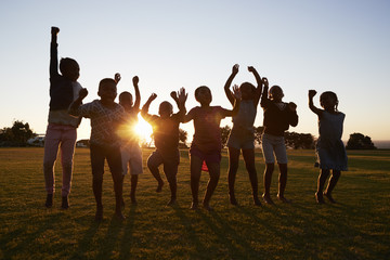 Silhouetted school kids jumping outdoors at sunset