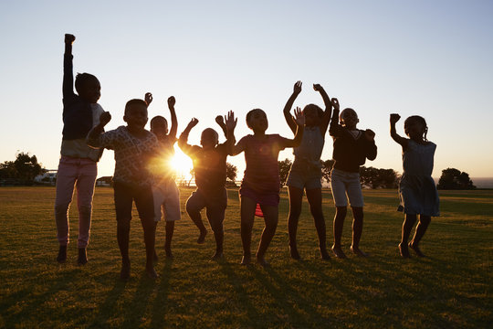 Silhouetted School Kids Jumping Outdoors At Sunset