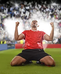 Foto op Plexiglas happy and excited football player in red jersey celebrating scoring goal kneeling on grass pitch © Wordley Calvo Stock