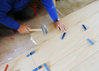 Construction worker using the rubber hammer to place a new stoneware porcelain tile floor in the...