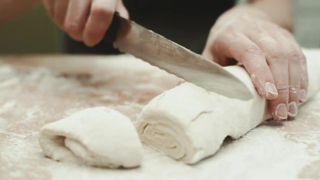 Close-up of female chef cutting raw dough on the board. Concept of dessert preparation.  