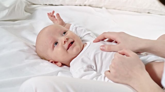 Closeup shot in slow motion of hands of mother stoking belly of cute baby lying on bed and touching his nose