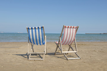 Two empty linen beach chairs one blue and one red in the middle of the image on the beach of Weymouth of the United Kingdom, facing the sea on a sunny day