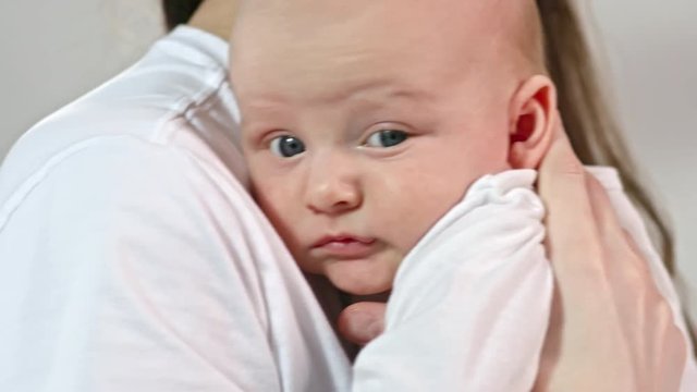 Tilt down of lovely baby looking at camera while mother holding him on arms and rocking
