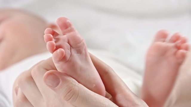 Closeup of loving mom caressing and kissing little baby foot