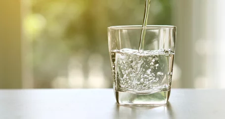 Wandaufkleber Nahaufnahme von gereinigtem frischem Trinkwasser aus der Flasche auf dem Tisch im Wohnzimmer © Cozine