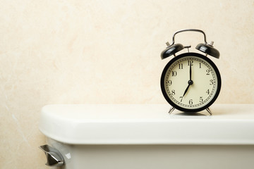 Naklejka premium black vintage alarm clock on toilet tank in the morning