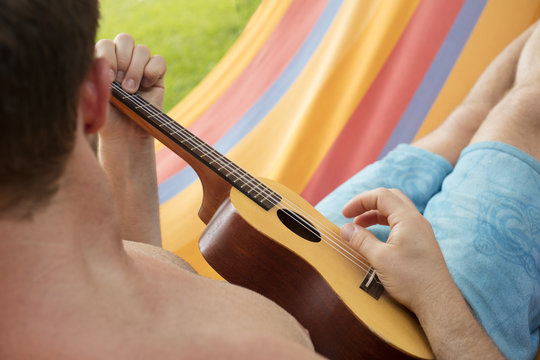 Detail of man relaxing on a hammock and playing ukulele