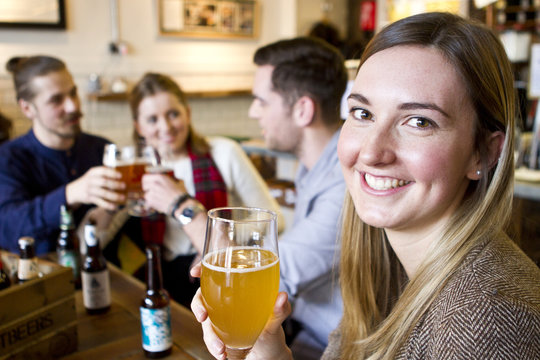 Young woman drinking beer in pub, friends in background, Dorset, Bournemouth, England