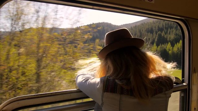 young caucasian woman travelling by train, looking out of the window at a scenic landscape
