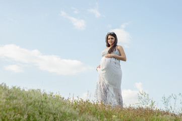 Pregnant woman in white dress, resting on a flowering meadow in summer