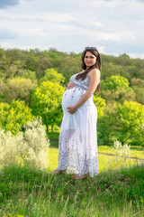 Fototapeta premium Pregnant woman in white dress, resting on a flowering meadow in summer