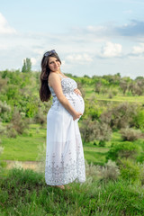 Pregnant woman in white dress, resting on a flowering meadow in summer