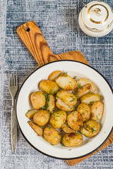 
 Potatoes.   Young fried potatoes on a white metal plate on a wooden cutting board.