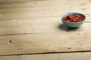 foto ampia di una ciotola azzurra con dentro salsa di pomodoro sopra tavolo in legno