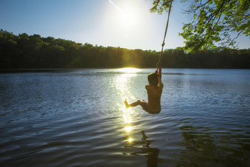 boy bungee jumping over water. kid swings on a rope and ready to jump into the water. Back view....