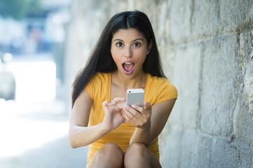 Shocked and surprised attractive young latin woman texting and talking on her smart cell phone